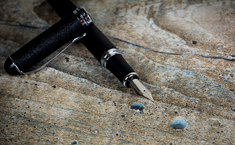 a black fountain pen with silver accents and a steel nib on a wooden tabletop